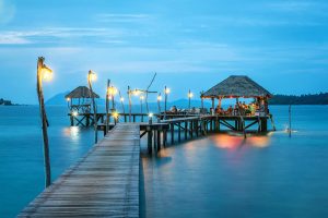 Illuminated pier and bungalow on a tranquil tropical sea at twilight.